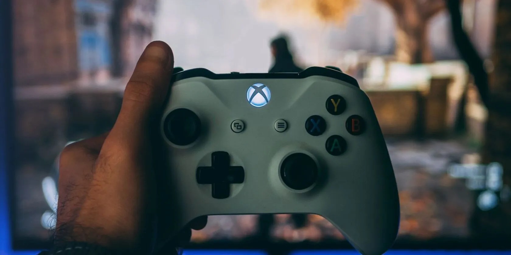 A photograph of a white Xbox controller in front of an illuminated monitor