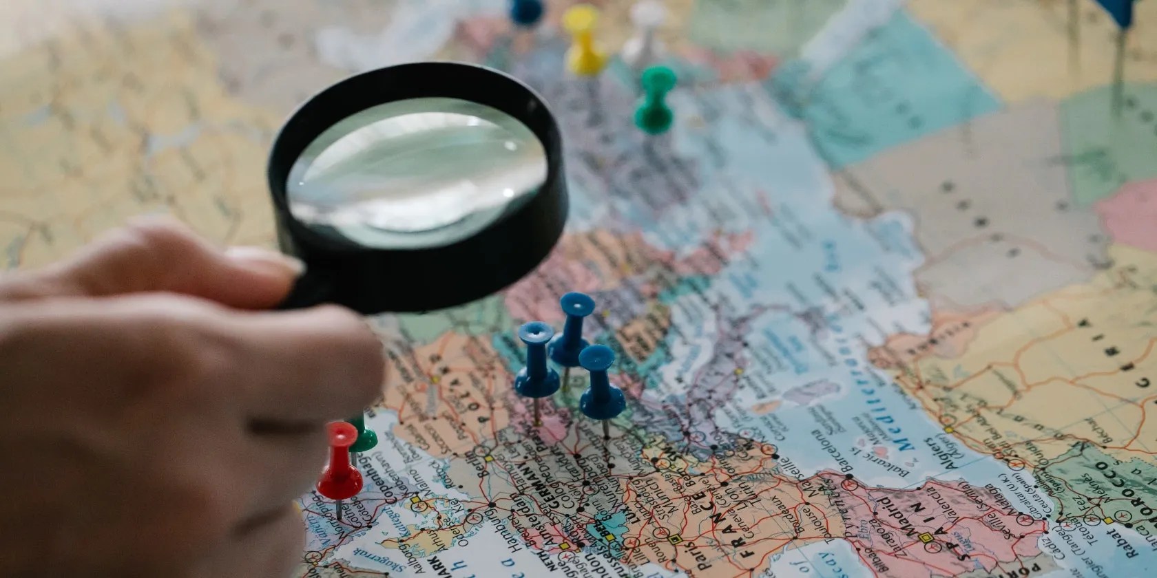 Hand with magnifying glass examining pins on a map
