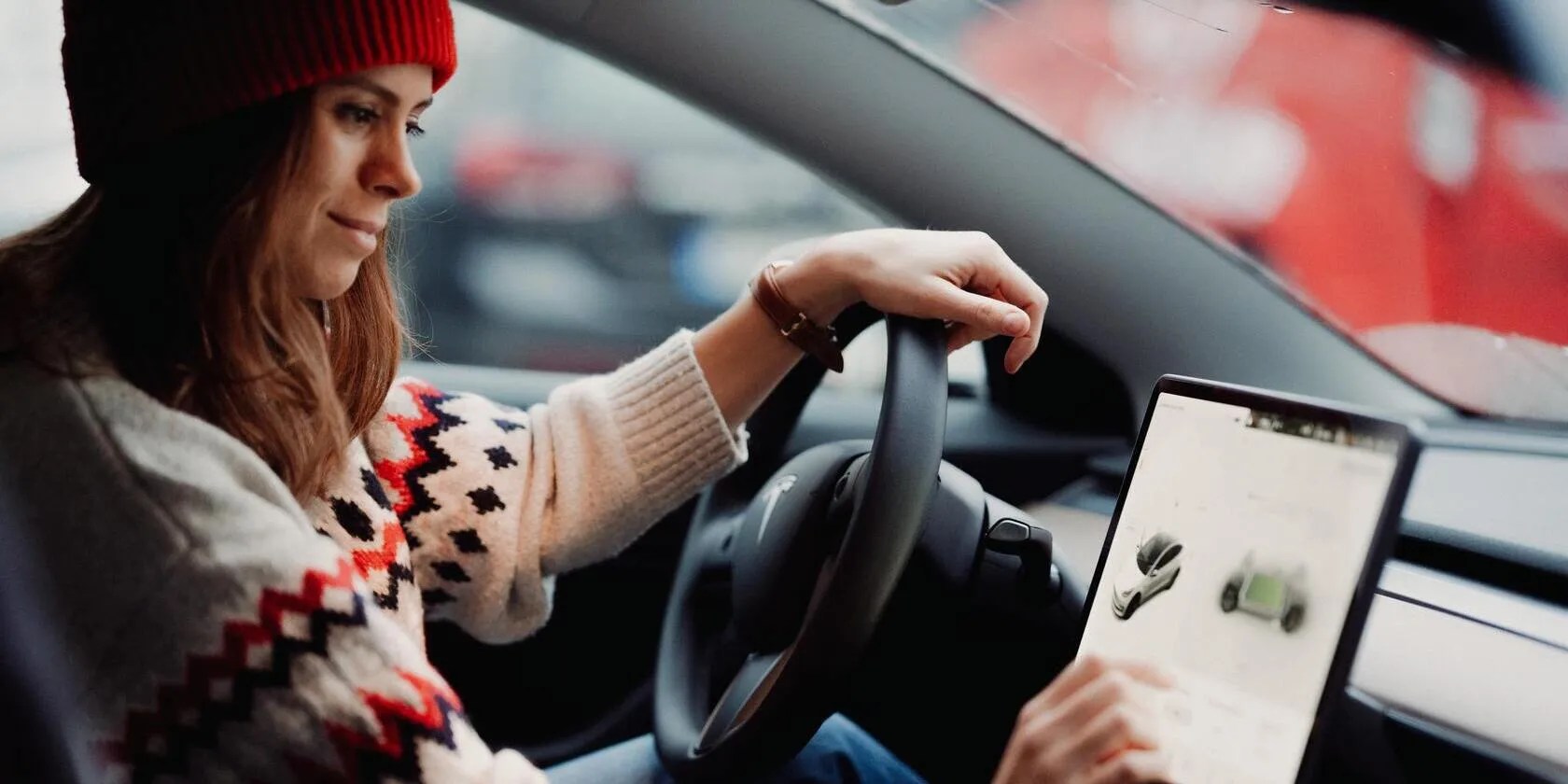 A Tesla driver wearing a sweater and hat uses their touchscreen.