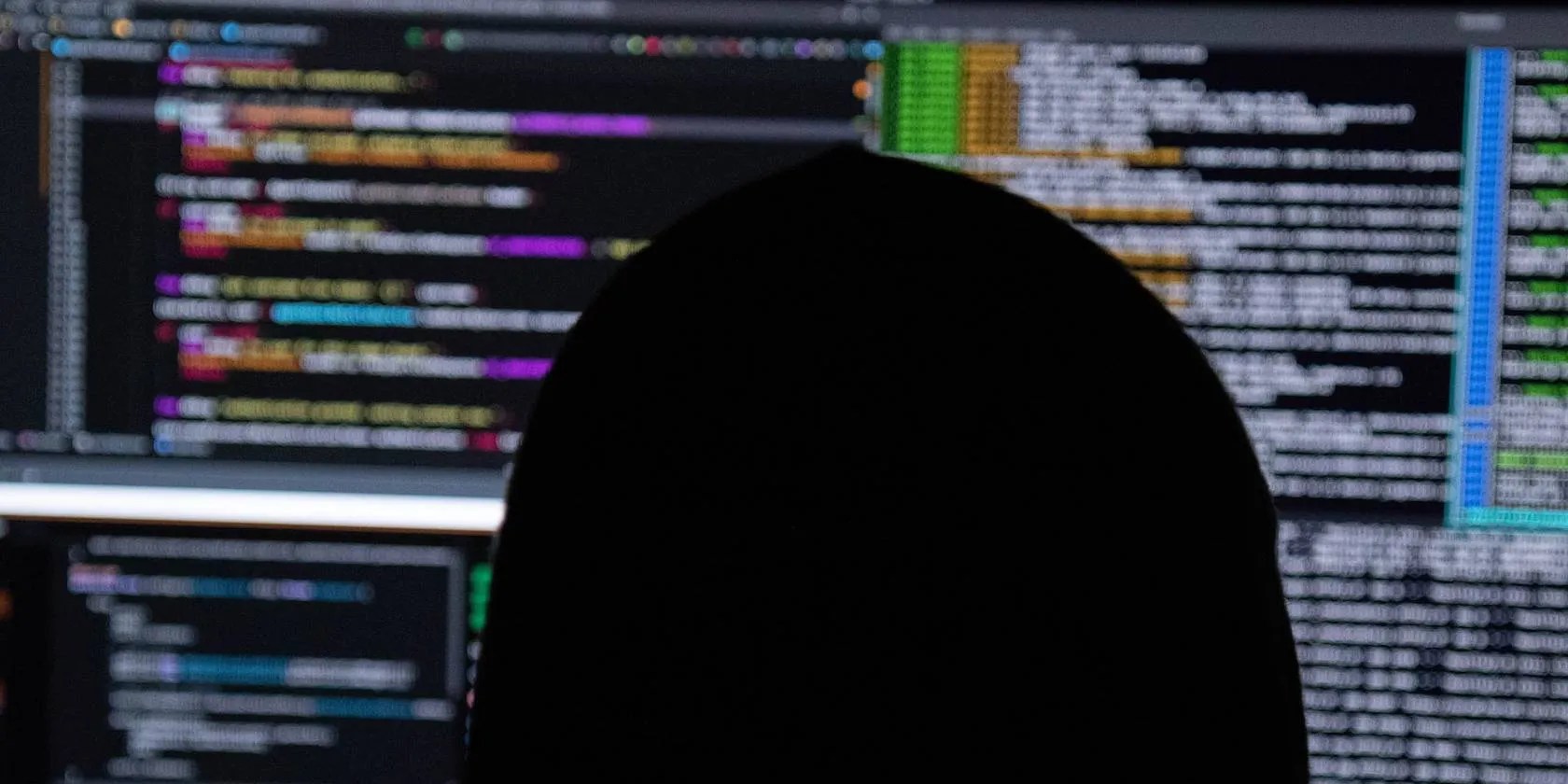 Hacker writing codes in front of computer screens