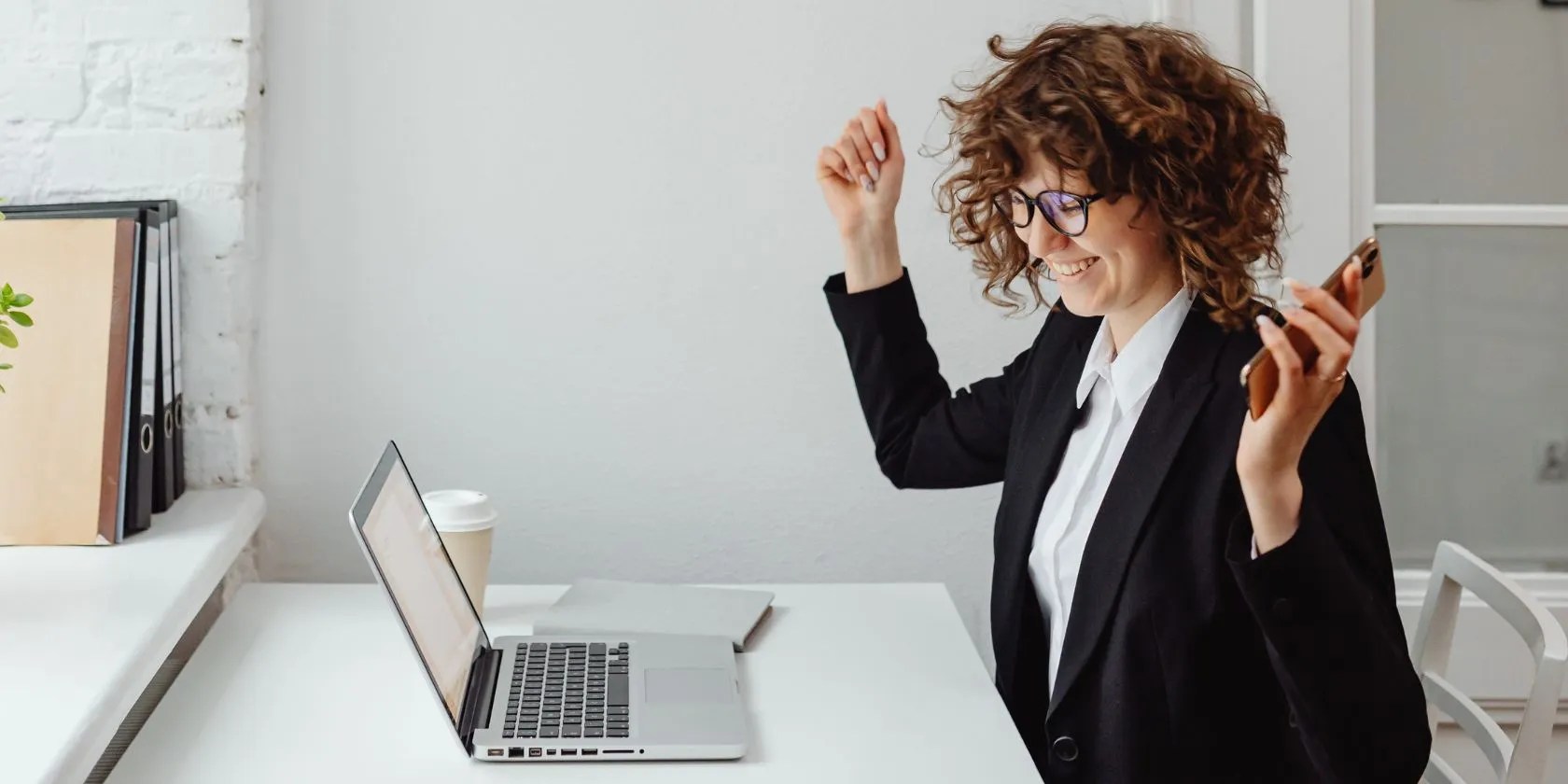 Woman celebrating with hands in the air in front of laptop on desk