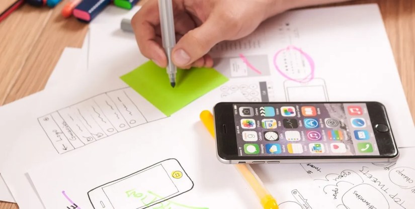 man drawing a navigation story board on paper with an iPhone on a table