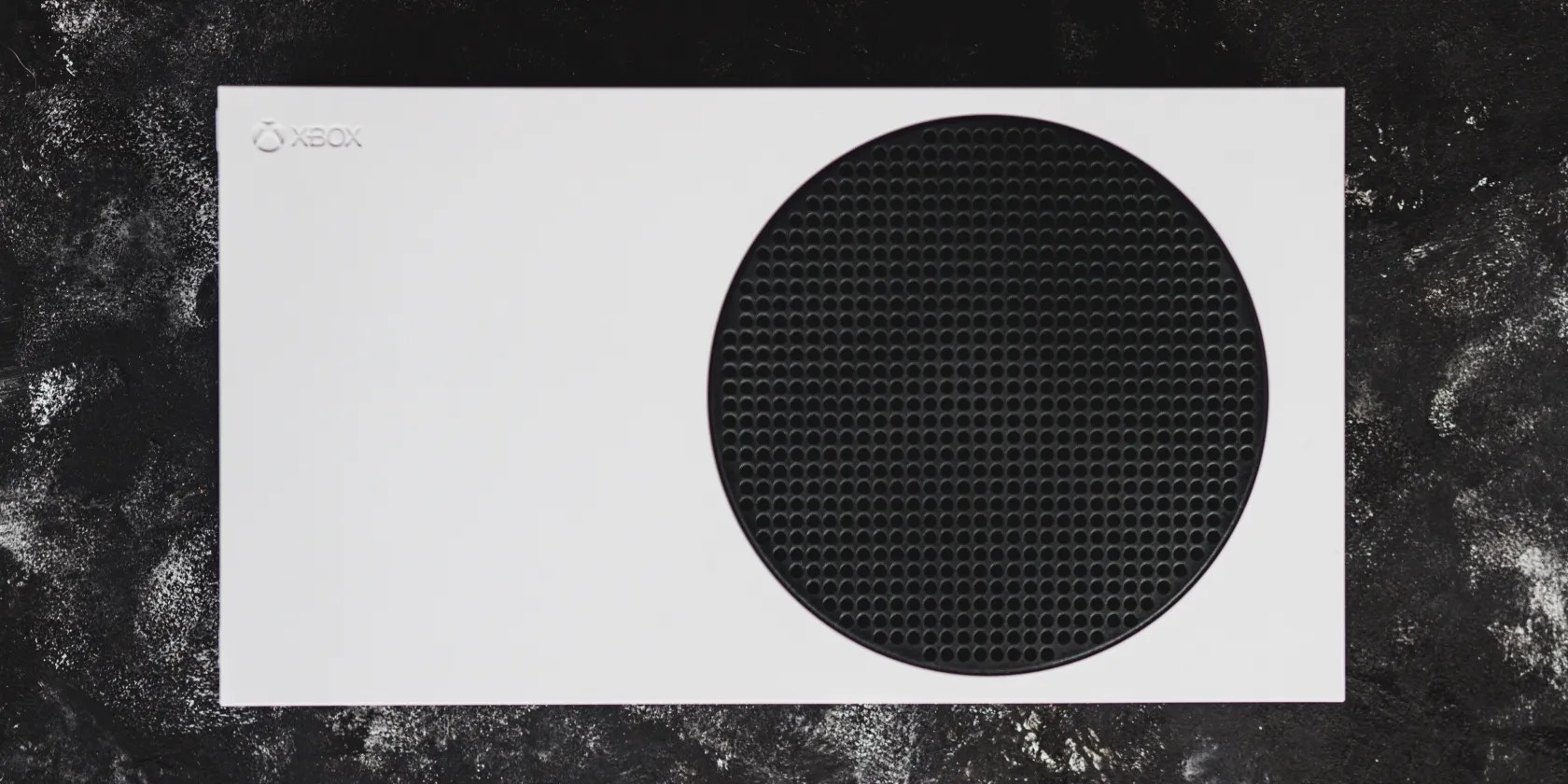 A photograph of an Xbox Series S console atop a black textured surface