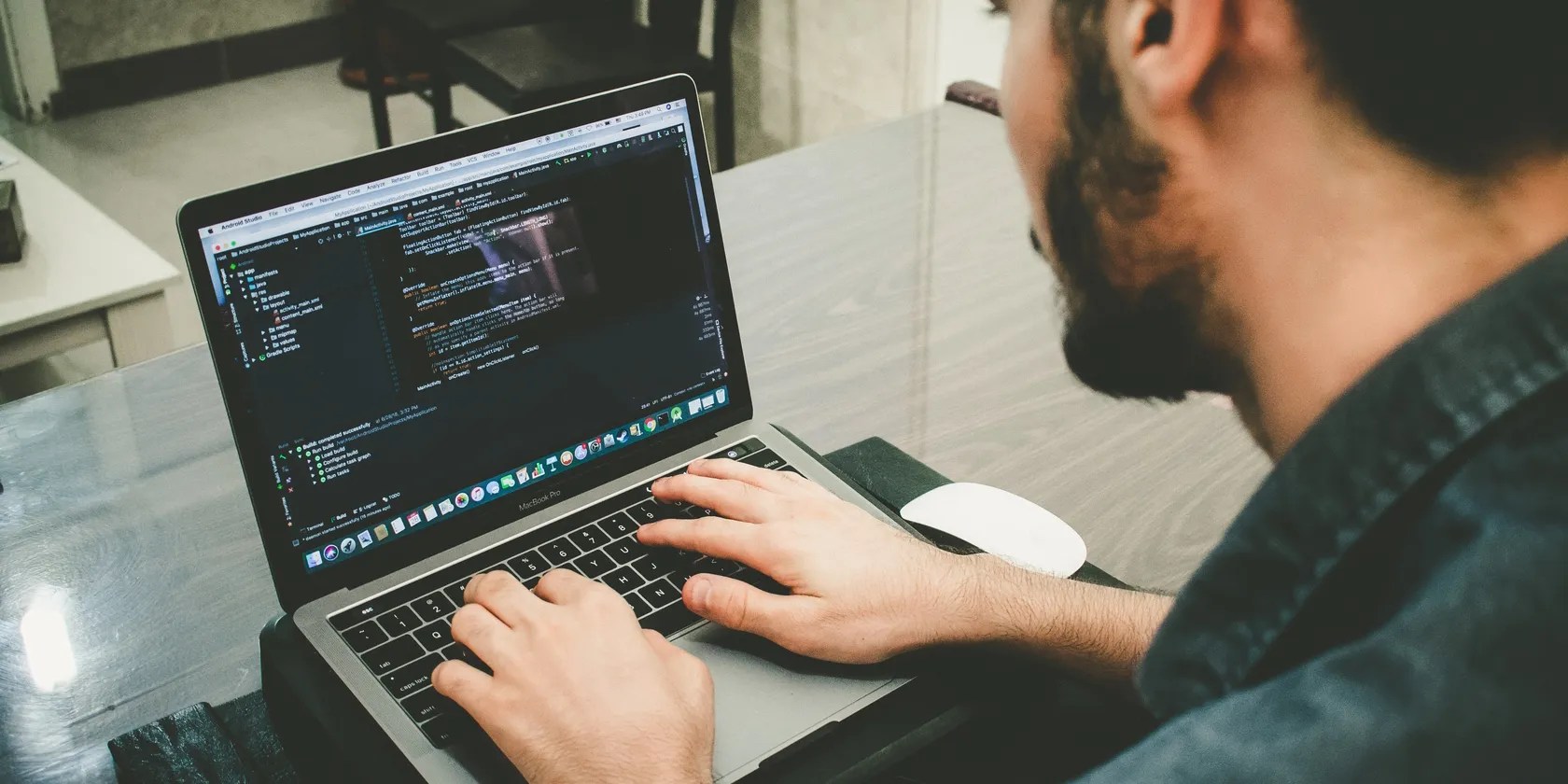 A man sitting at a desk typing on a laptop with code on the screen.
