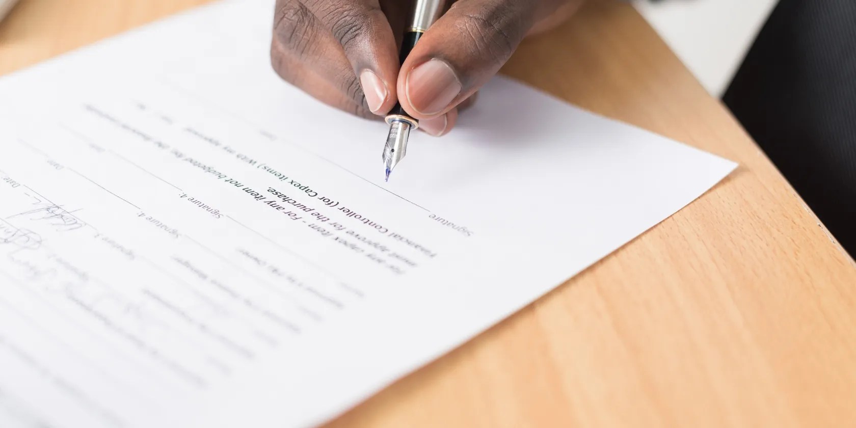 A man’s hand holding a pen signing a document.