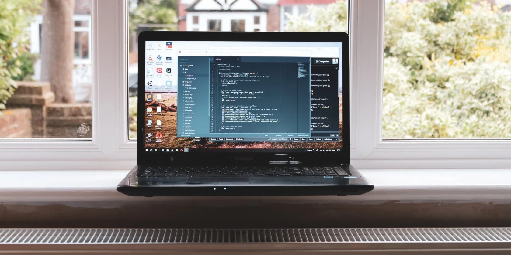 An open laptop sitting on a windowsill with a residential view in the background.