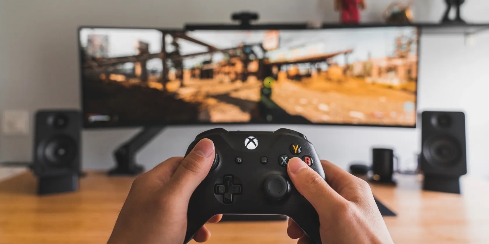 A photograph of a person holding an Xbox Wireless Controller in front of a monitor