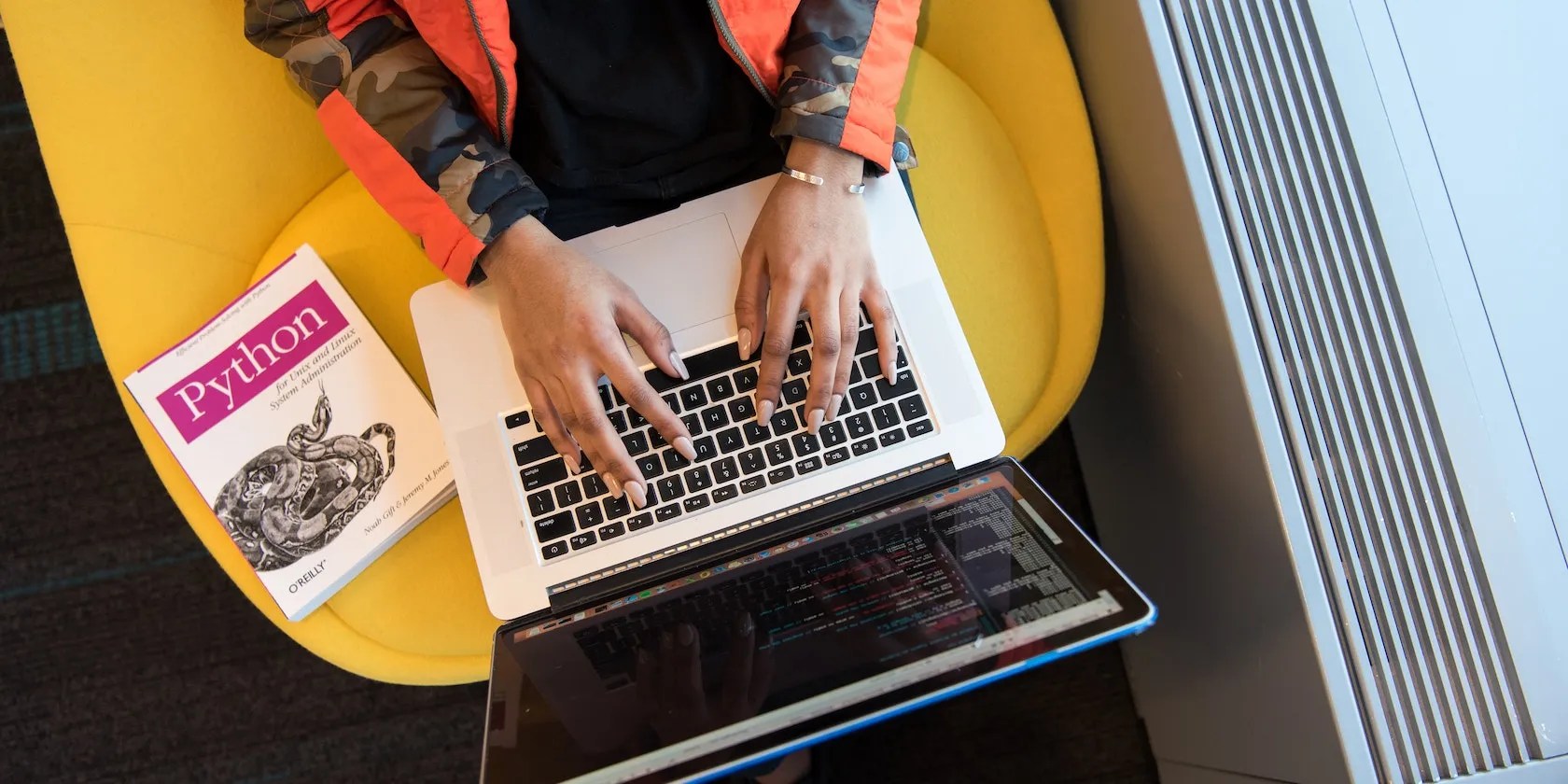A person using a MacBook laptop with a Python book on the chair