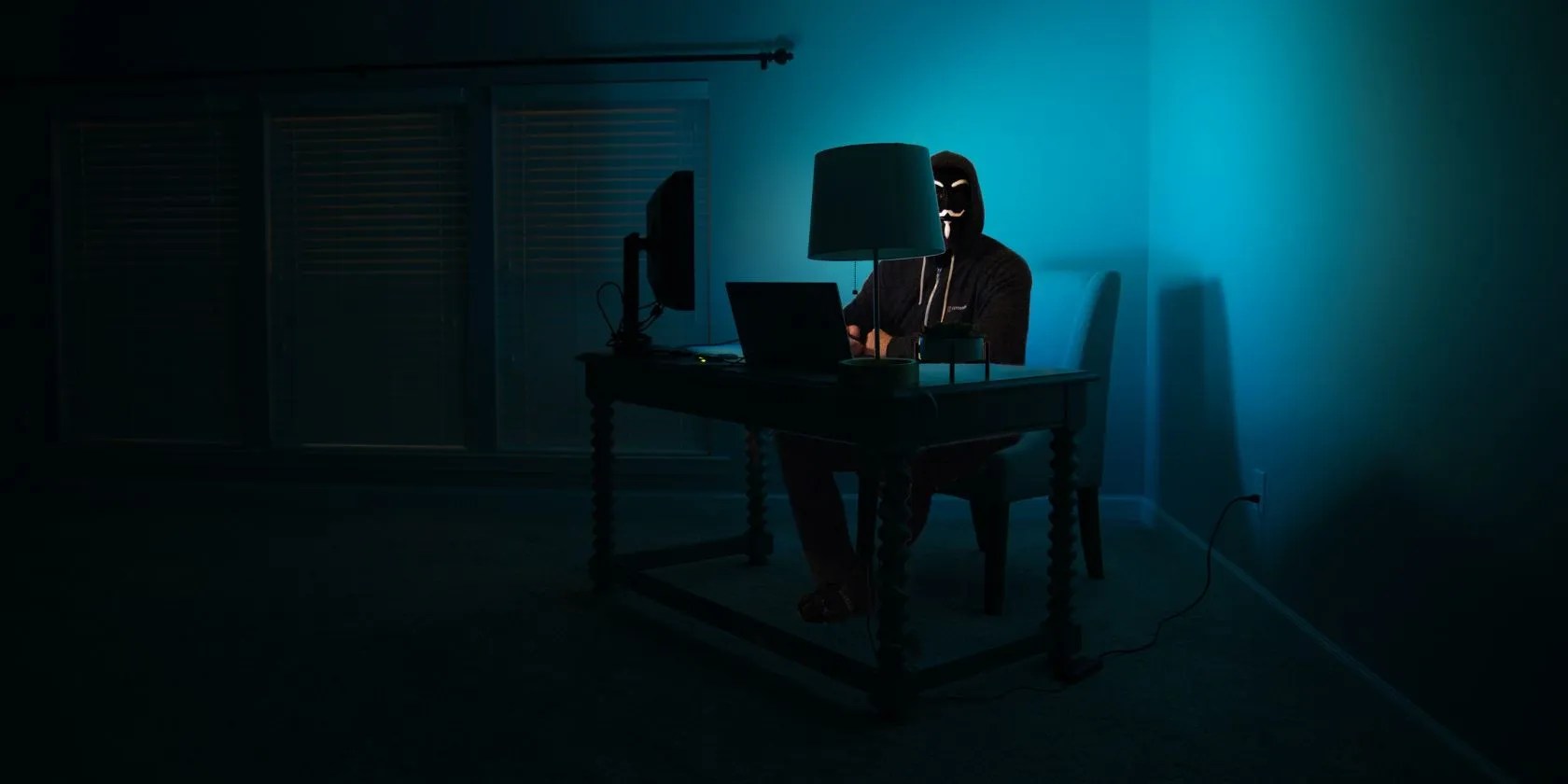 masked individual sitting at computer in dark room