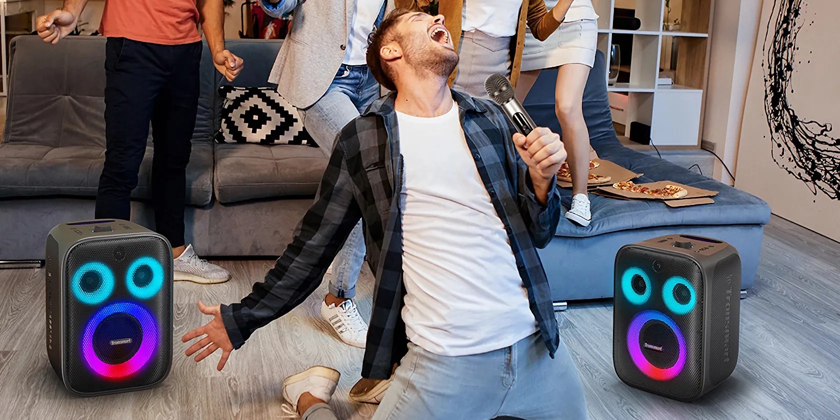 tronsmart speakers on the floor with man on his knees singing into microphone