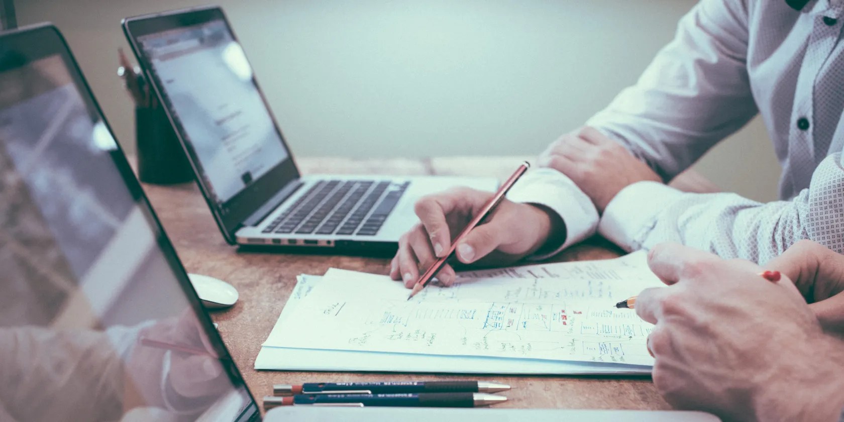 Two men setting at two MacBooks with a paper between them