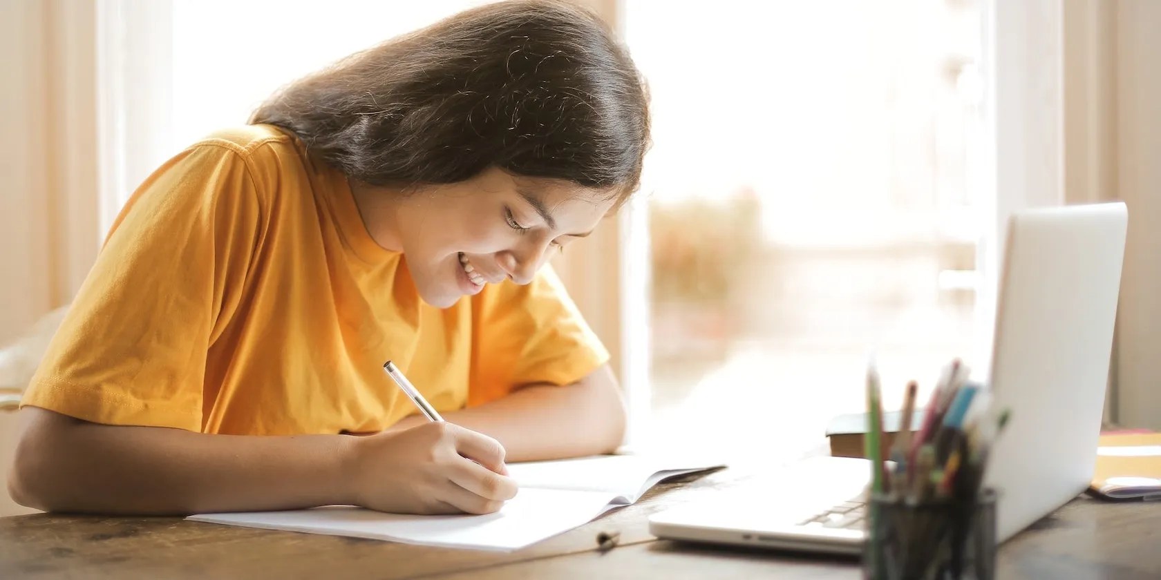 Woman writing on the table in front of a laptop