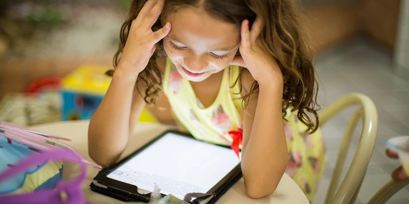 child sittting at table using tablet to read