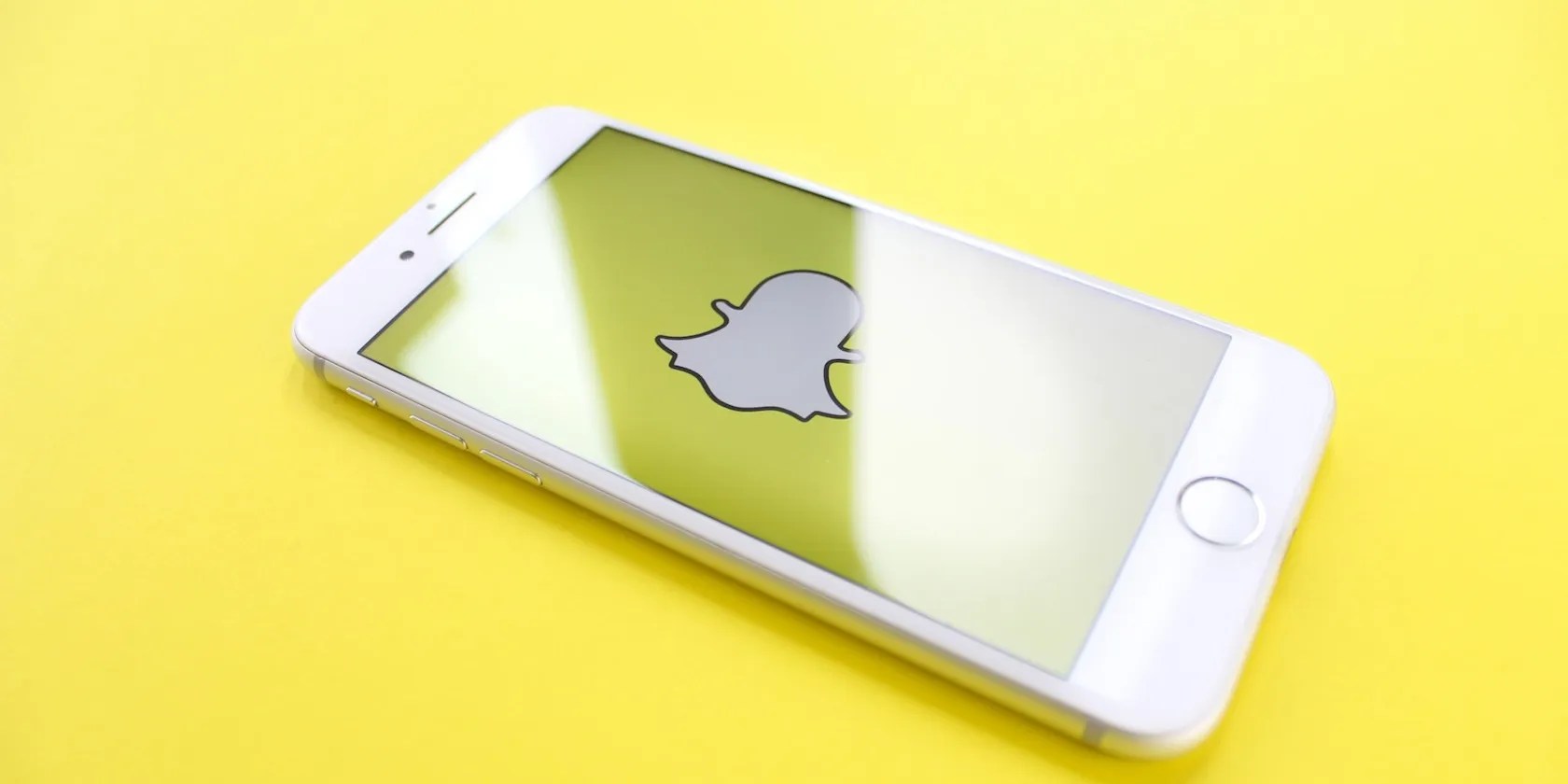 A silver iPhone 6 on a yellow surface with snapchat on