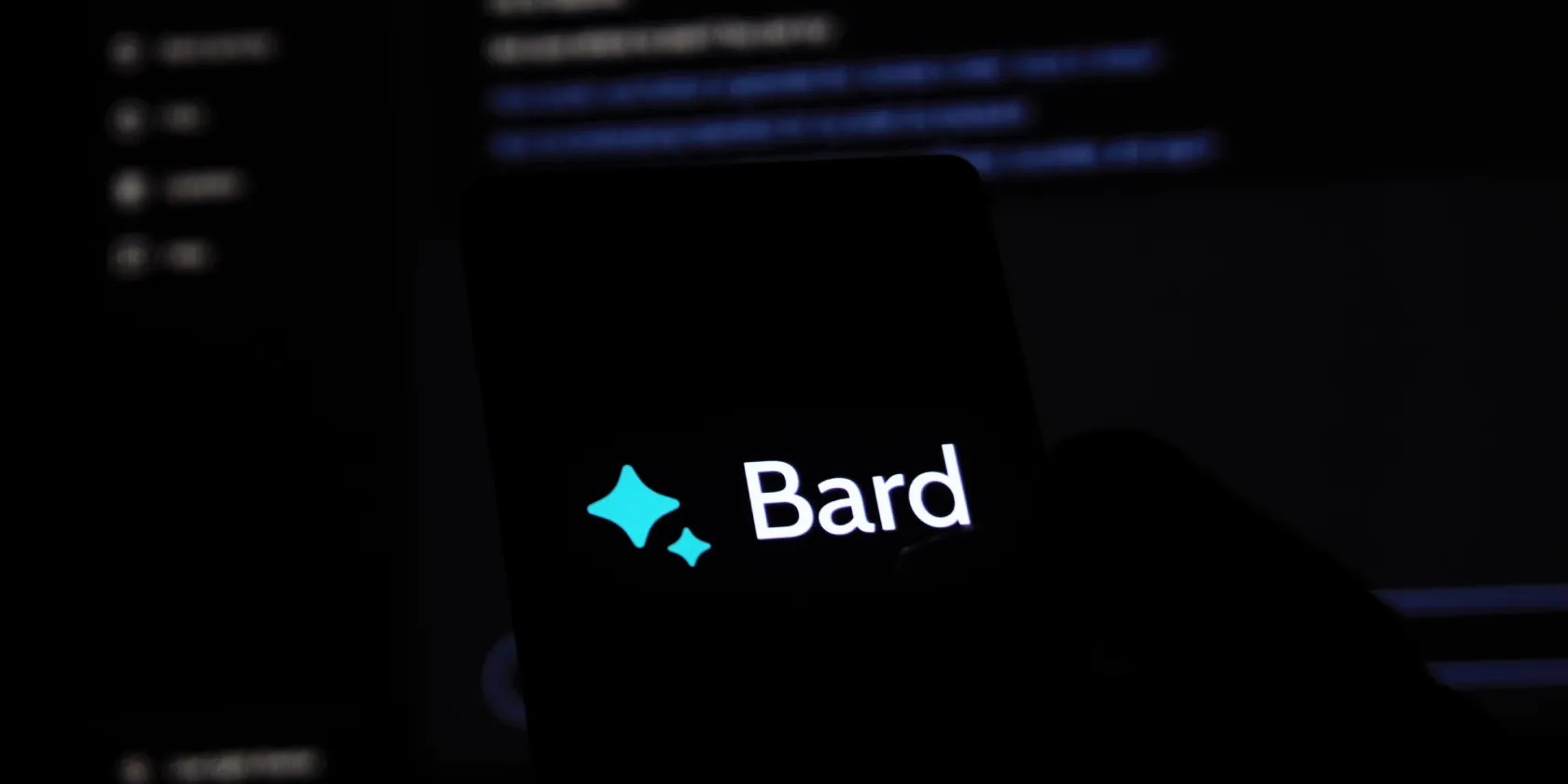 Using Google Bard on a smartphone with a laptop screen in the backdrop
