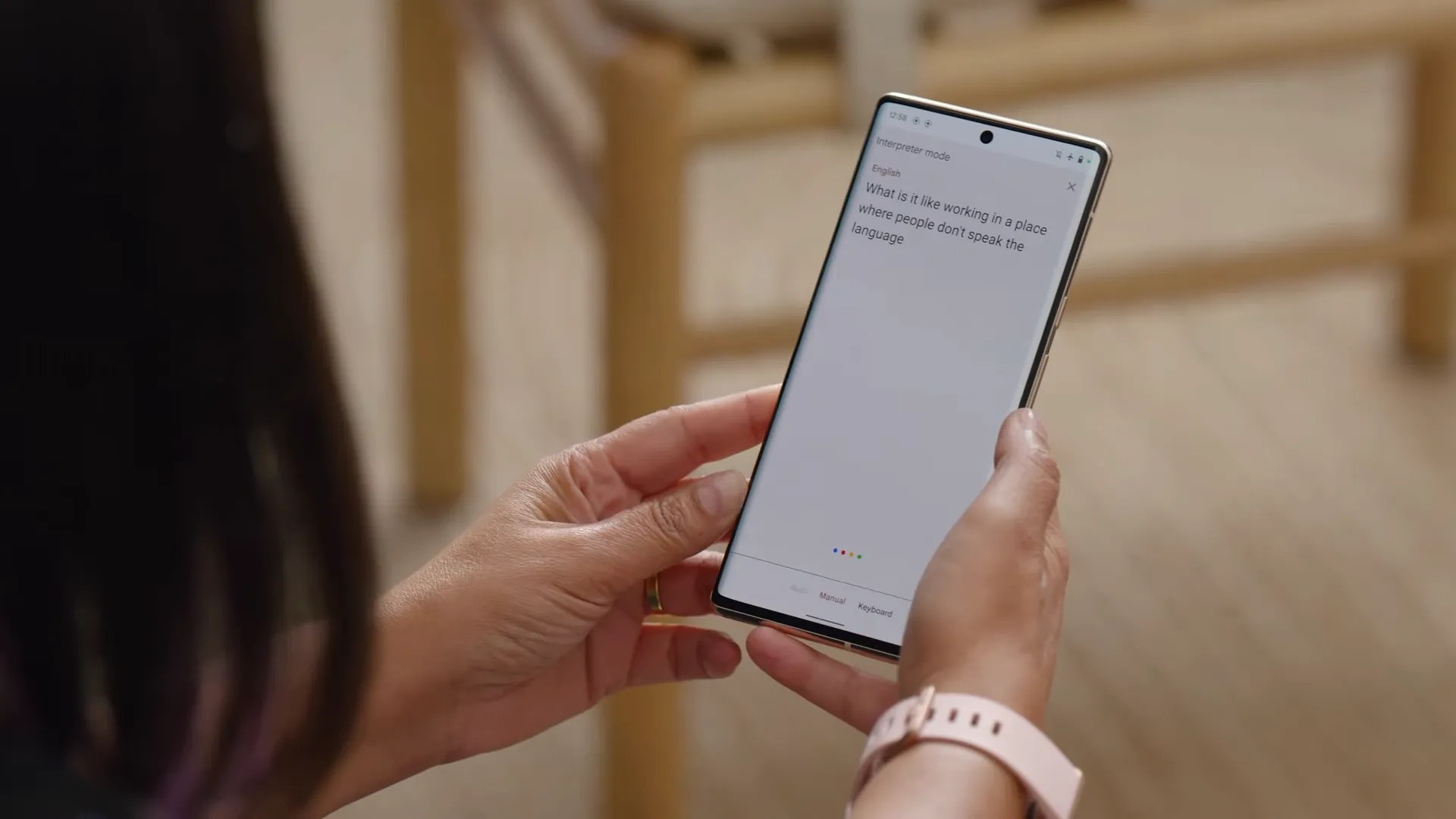 A person wearing a watch with a pink band holds a Google Pixel phone and looks at a translation.