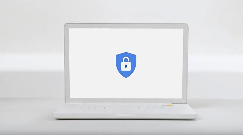 A white laptop sits on a white table. The Google Advanced Protection Program logo is on the laptop&rsquo;s display