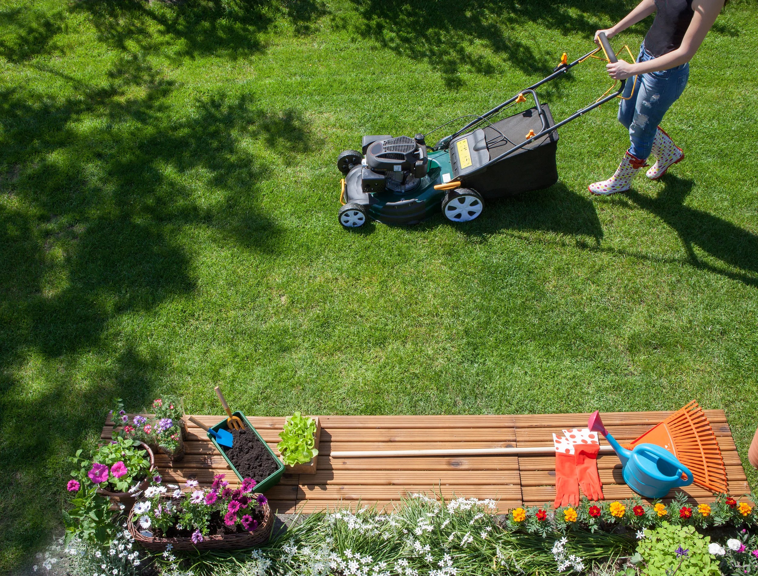 Woman wearing wellington boots mowing grass with lawn mower in the garden, gardening tools