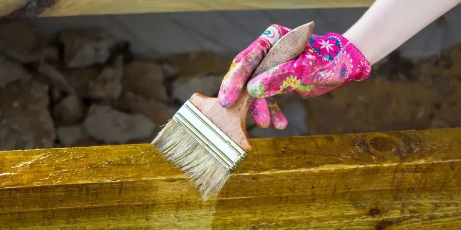 Woman wearing glove holding a brush as she&rsquo;s staining a beam.