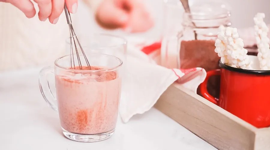 Mixing hot chocolate mix in glass cup with with small whisk