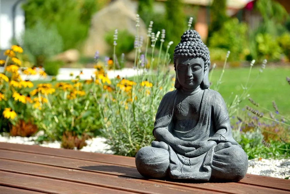 A closeup of a small Buddha statue in a garden with a blurry background