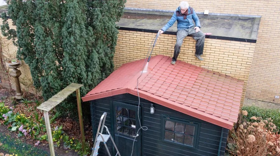 senior man cleans roof of shed