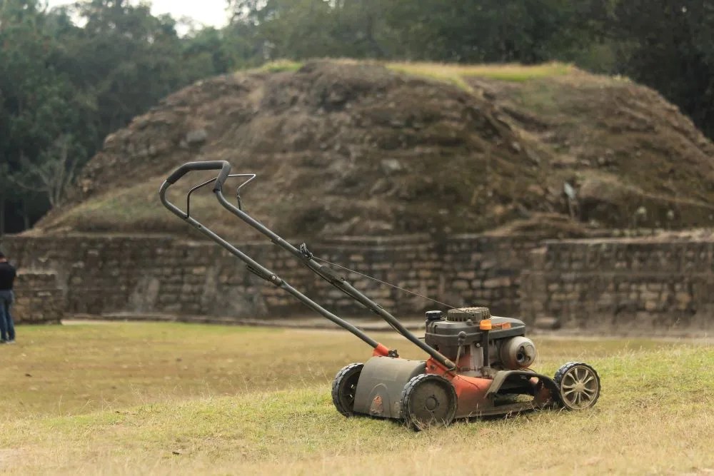 An old lawn mower sits on a field before a hill