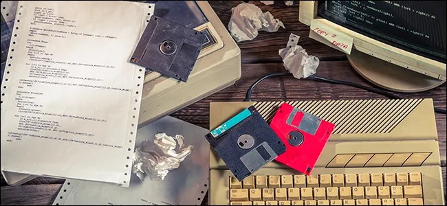 A desk full of floppy disks, old computer hardware, and crumpled up paper.