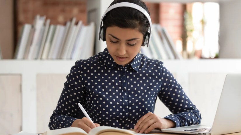 A woman wearing headphones writes in a notebook.