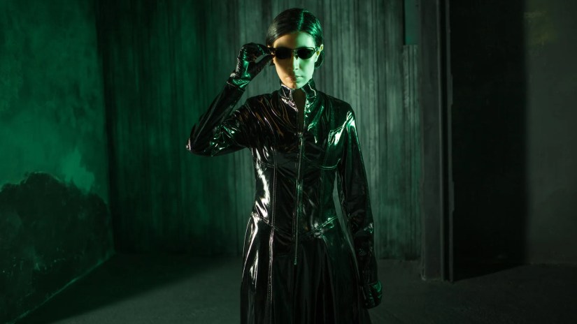 A young woman dressed like the character Trinity from &lsquo;The Matrix&rsquo; surrounded by green hues.