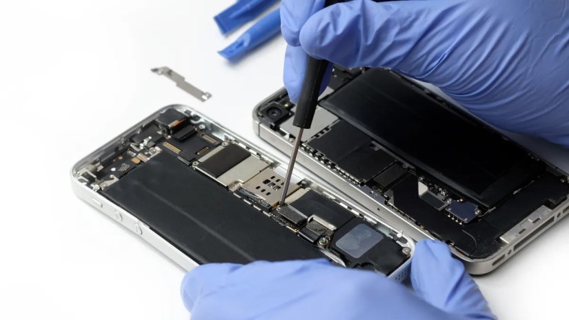 Closeup of technician&rsquo;s gloved hands repairing an iPhone&rsquo;s internal parts.