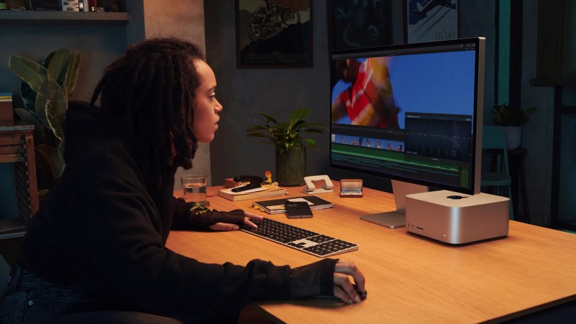 An artist using the Mac Studio with a Studio display. The computer fits snugly under the display.