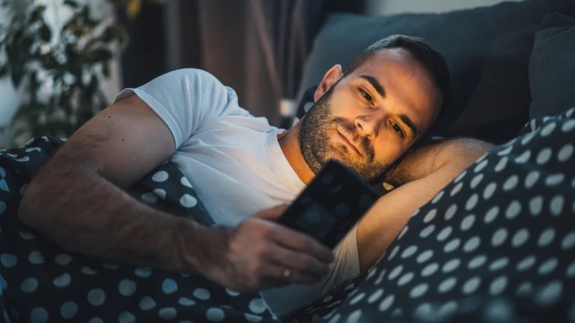 A man using a smartphone while lying in bed.