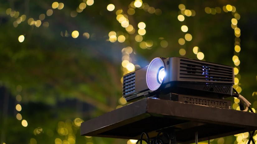 A projector on a stand far away from the screen
