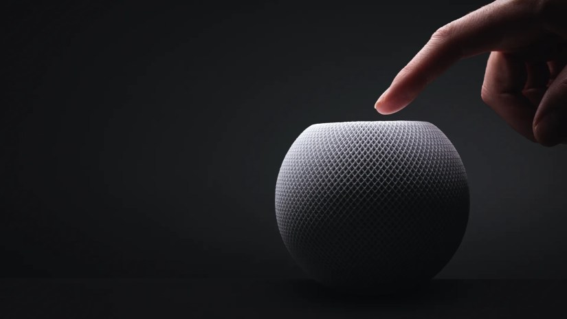 Someone&rsquo;s hand touching an Apple HomePod mini against a black background.