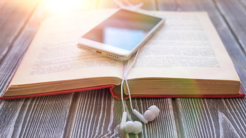 A smartphone on top of an open book with dangling earbuds