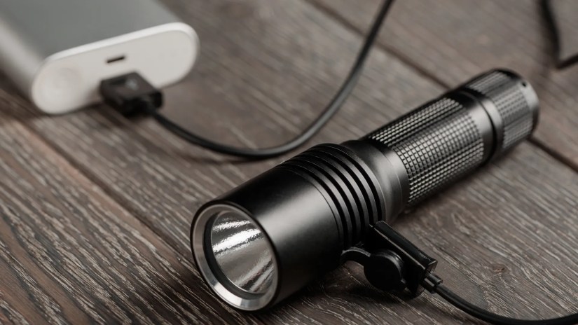 Rechargeable flashlight on a table connected to a battery.