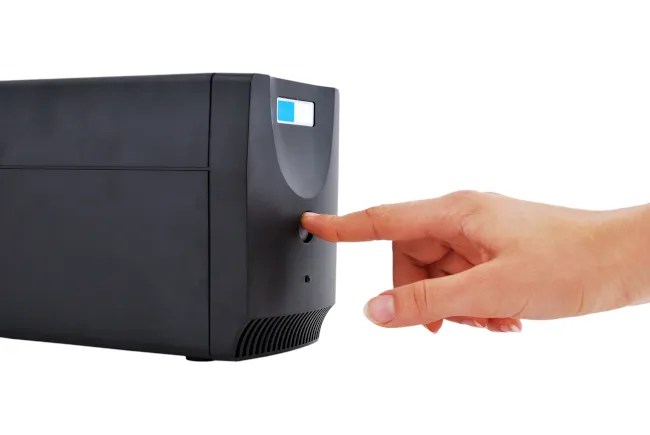 Person&rsquo;s hand pressing a button on an uninterruptible power supply (PSU).