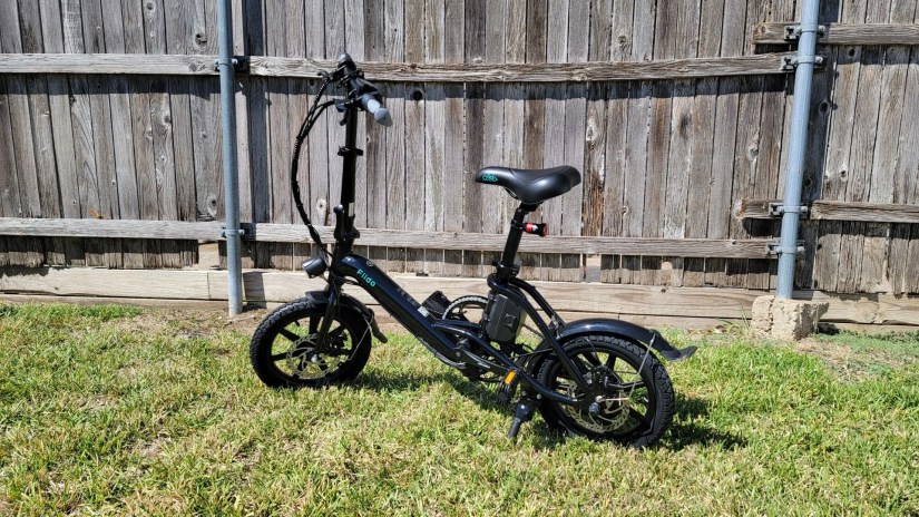Fiido D3 Pro Mini Electric Bike standing in the grass next to an old wooden fence
