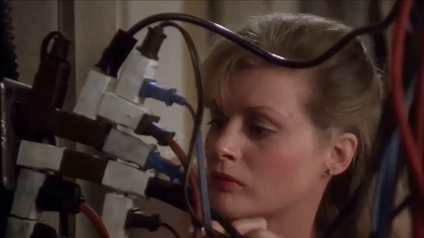 A woman looks at an outlet overloaded with extension cords.