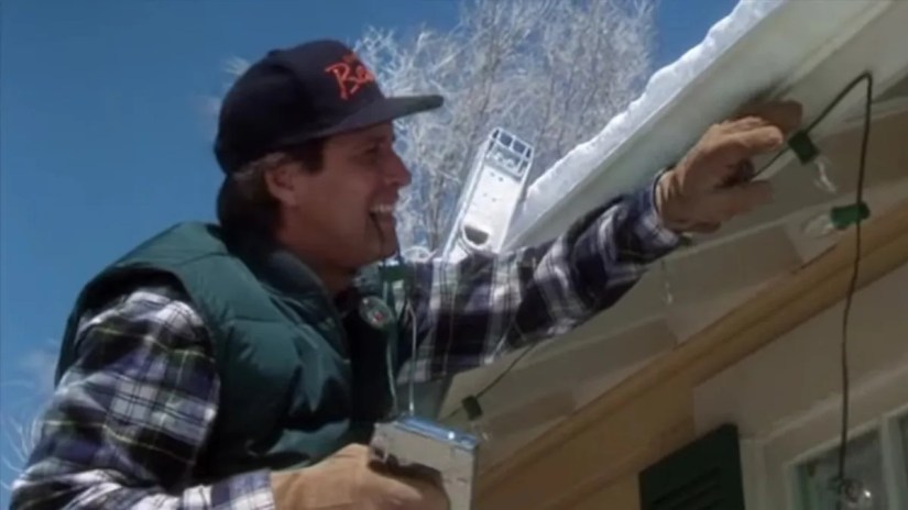 A man staples his hand to his gutters trying to hang Christmas lights.