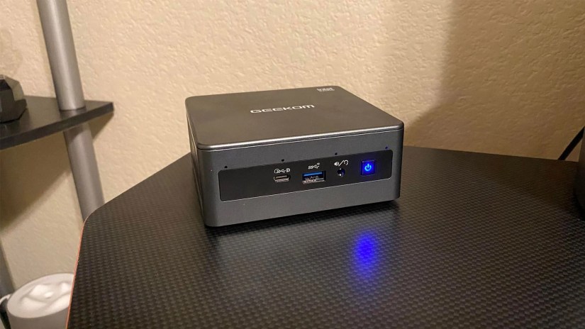 GEEKOM Mini IT11 PC front-facing on a black desktop.