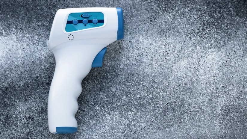 A forehead thermometer sitting on a gray table.