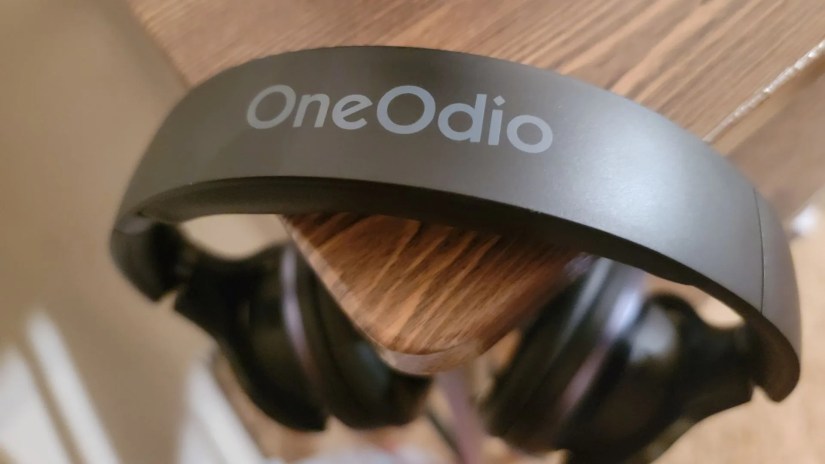 Logo on top of OneOdio A10 Hybrid ANC Headphones hanging from desk corner