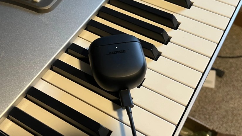 Bose QuietComfort 2 earbuds case charging on piano