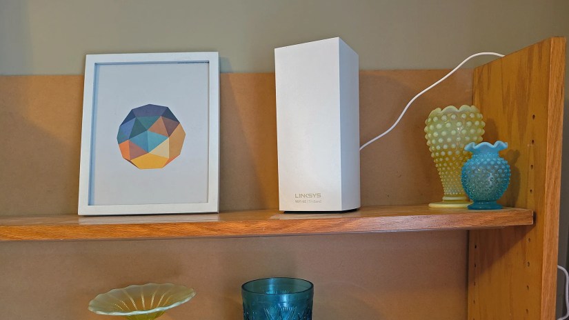 The LinkSYS Atlas 6E router on a shelf between a vase and a picture