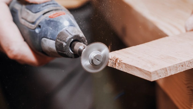 Man holding a rotary tool cutting wood.