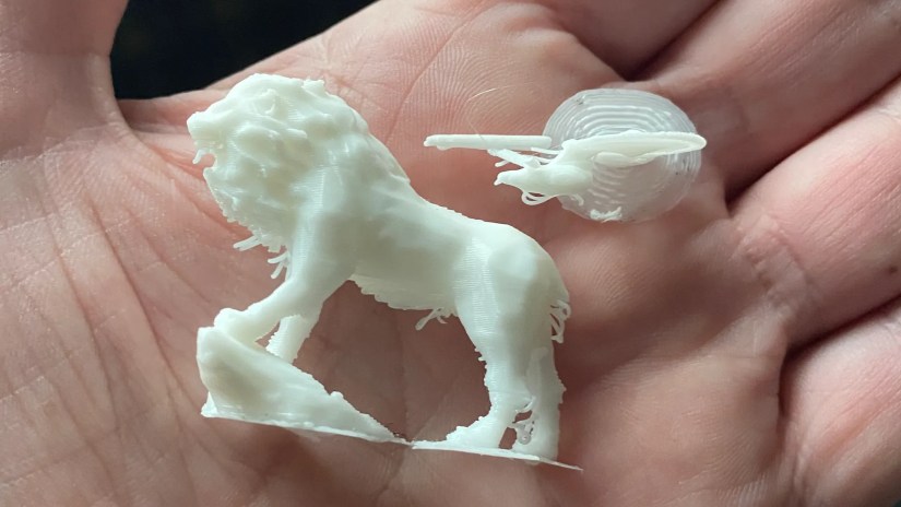 A man&rsquo;s hand holding a 3D printed lion and a small model of the Starship Enterprise.