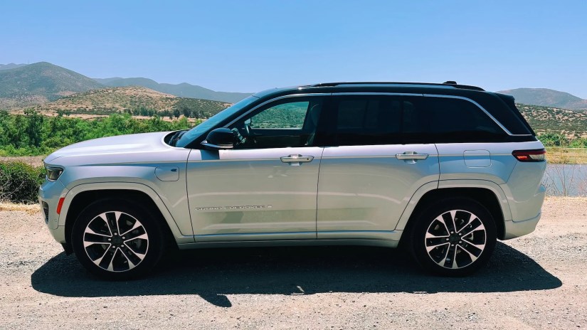 A side view of the Jeep Grand Cherokee 4xe in silver in front of a lake