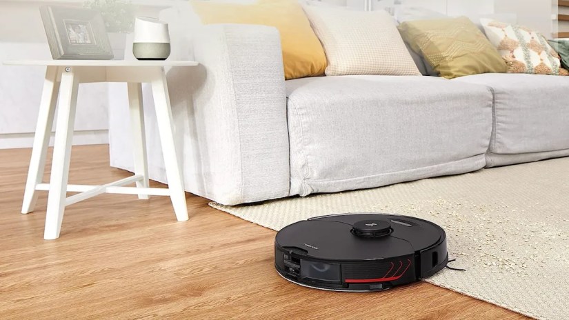 Round black robot vacuuming cleaning up a spill on a cream-colored rug.